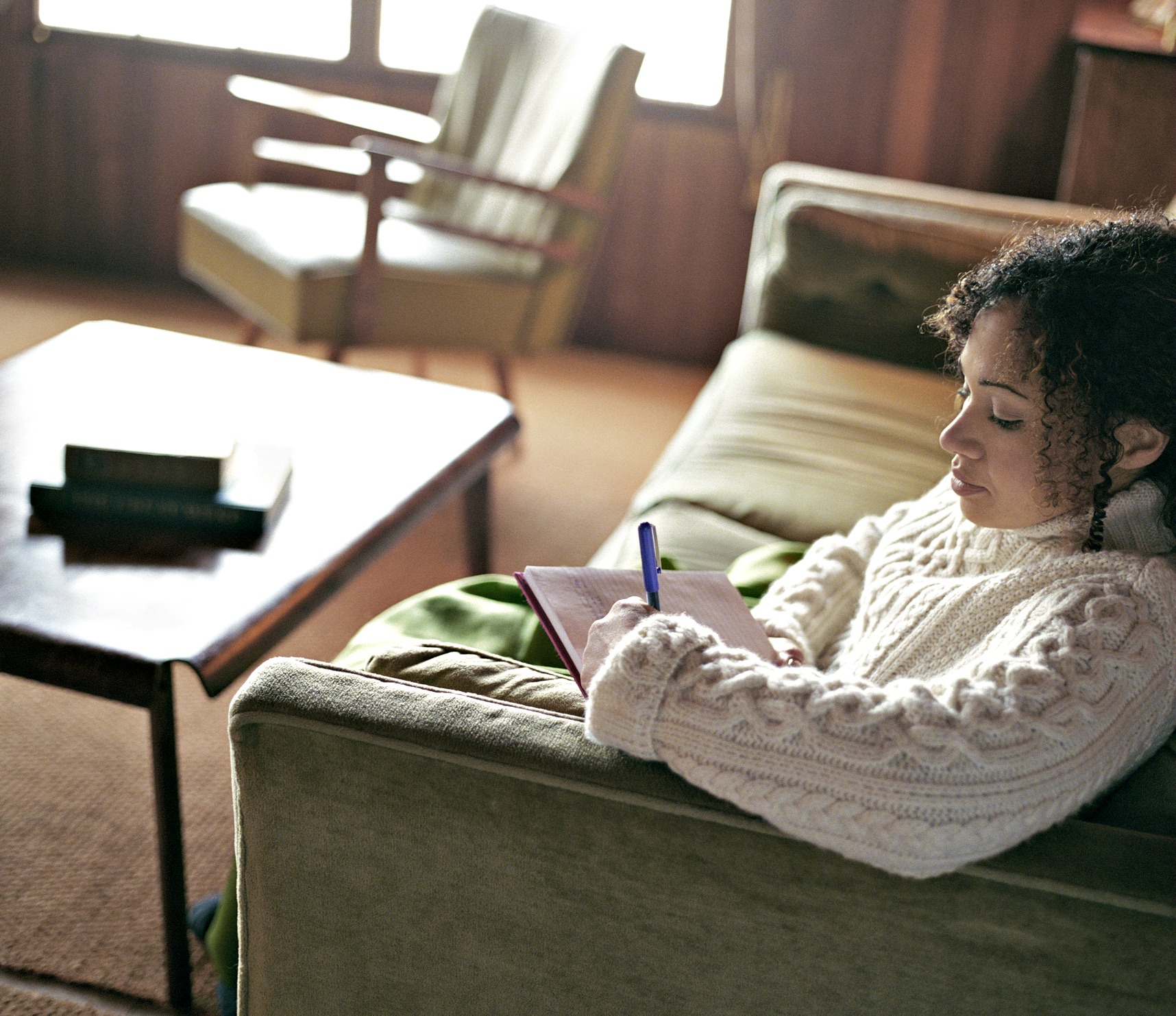 Woman sitting on couch writing self-reflections about her psychotherapy and counseling session.