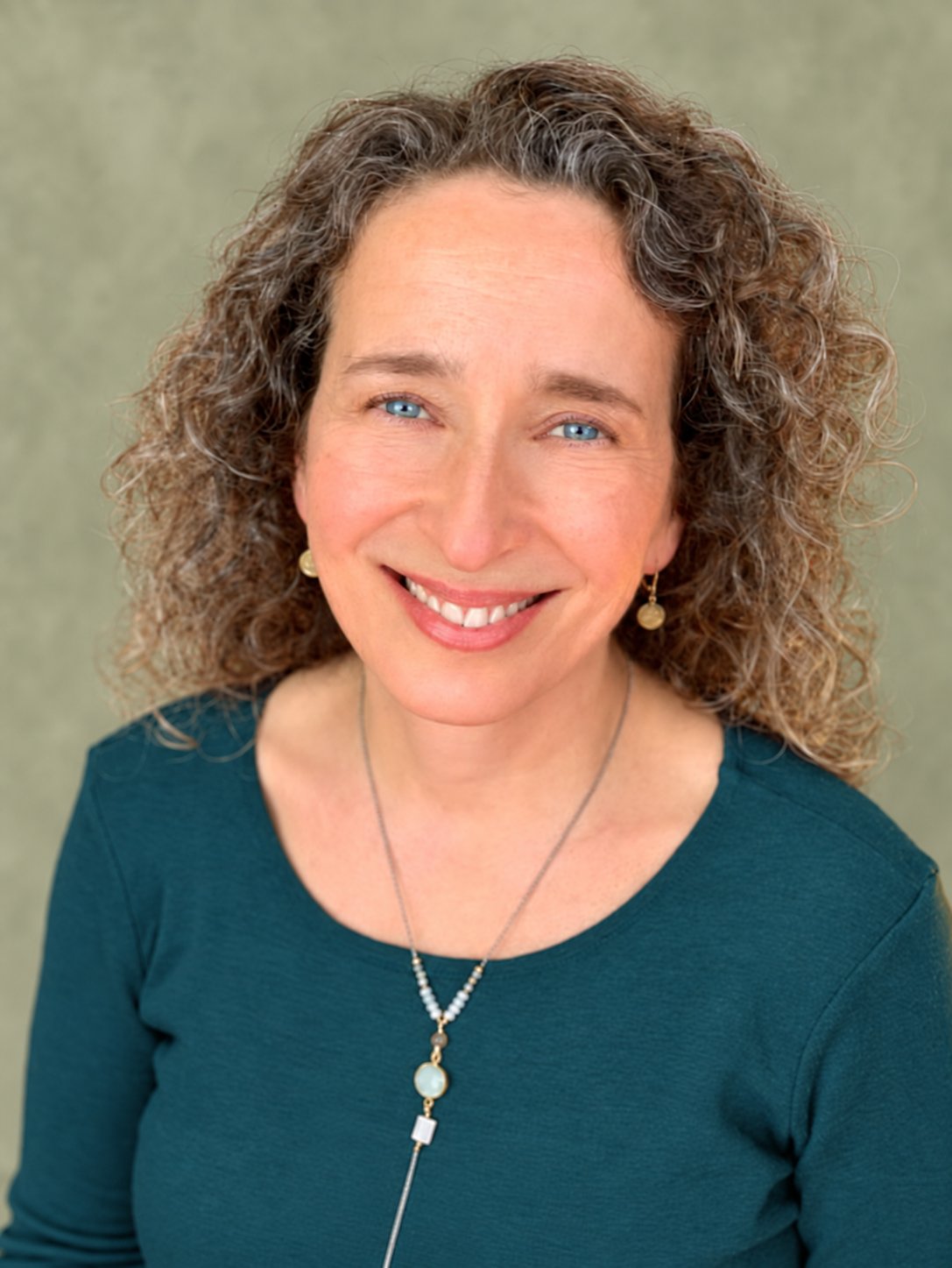 Meet Lucrezia Mangione — Mind Body Well Therapy Lucrezia Mangione smiling in a deep teal top against a soft sage background.